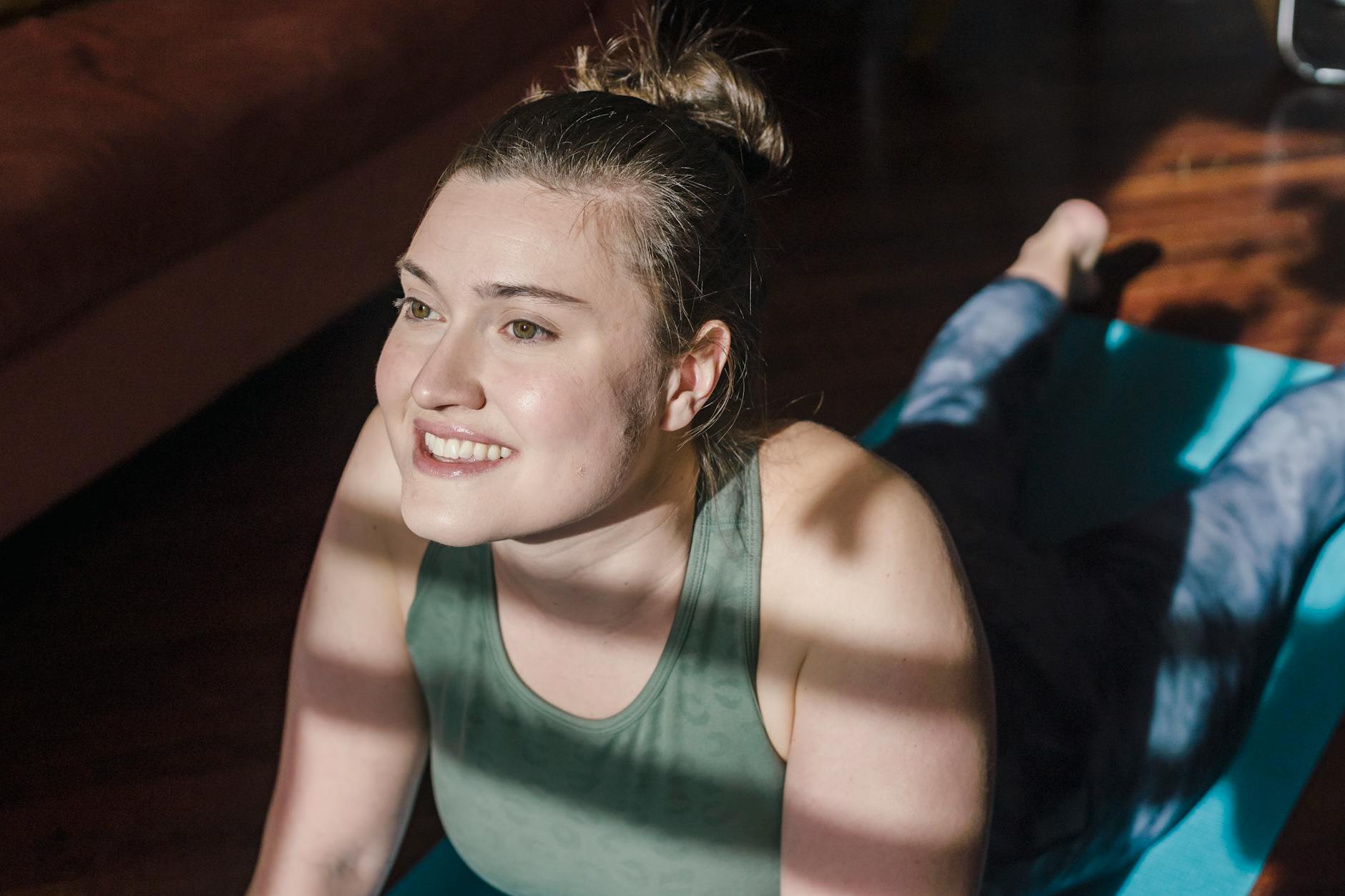 A person in comfortable clothes stretching on a yoga mat in a sunlit room.